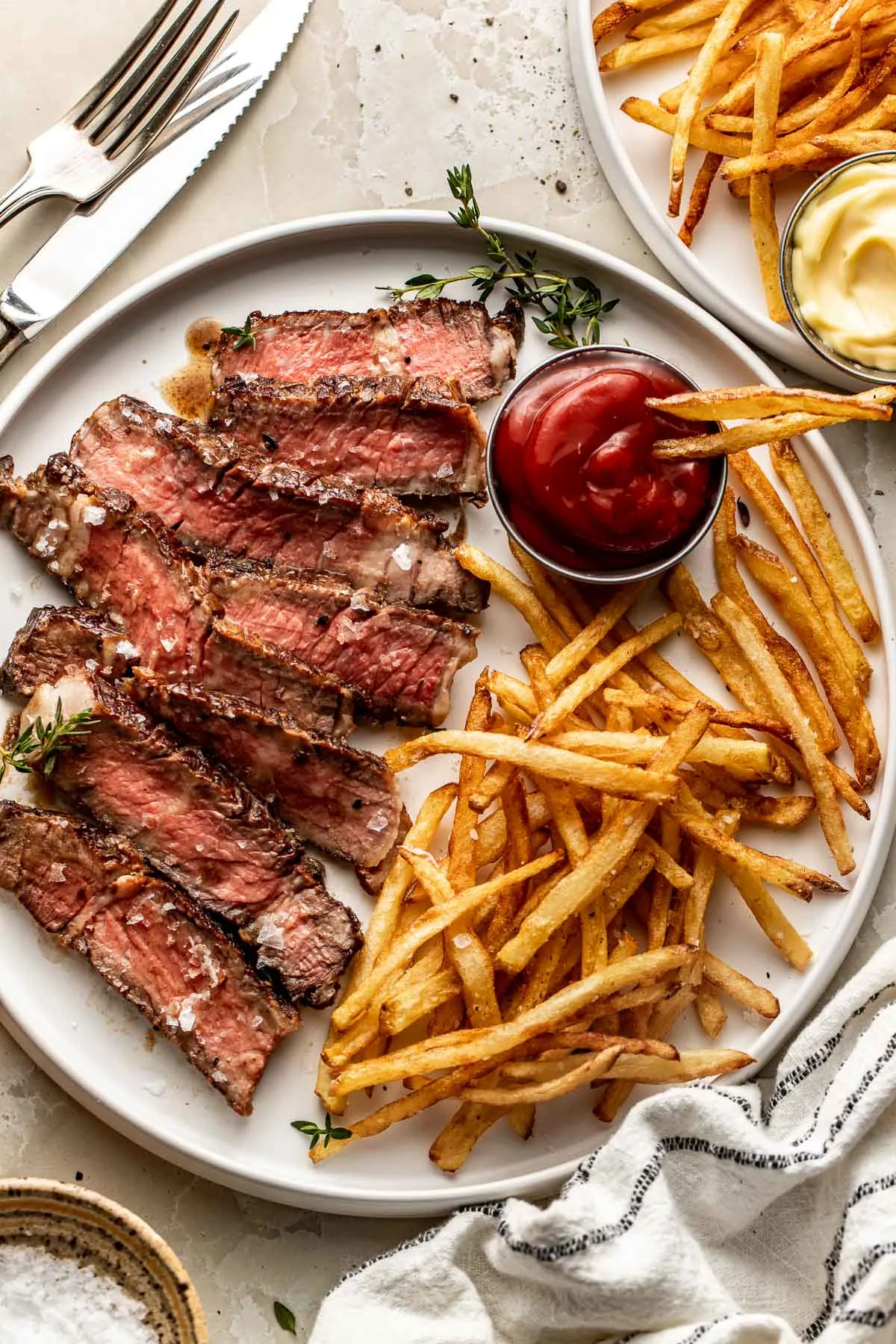 Skivad stekt biff med tunna pommes frites, ketchup och timjan på en vit tallrik