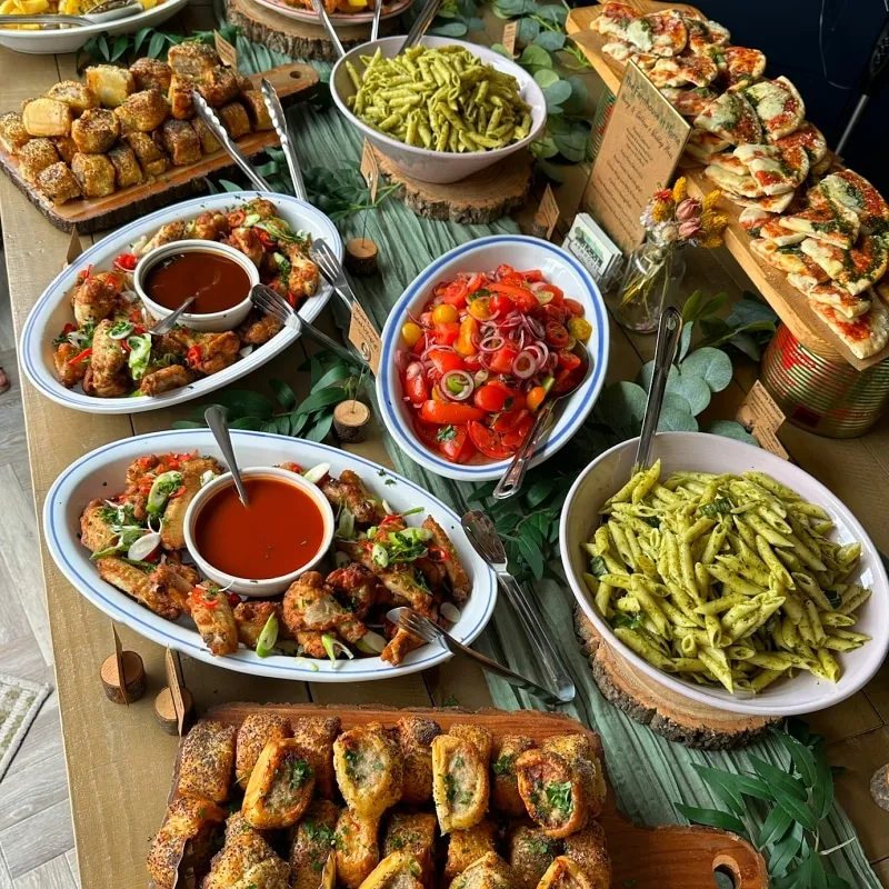 Buffébord uppifrån med kycklingvingar, pastasallad, tomatsallad, focaccia och små bakverk på träbrickor