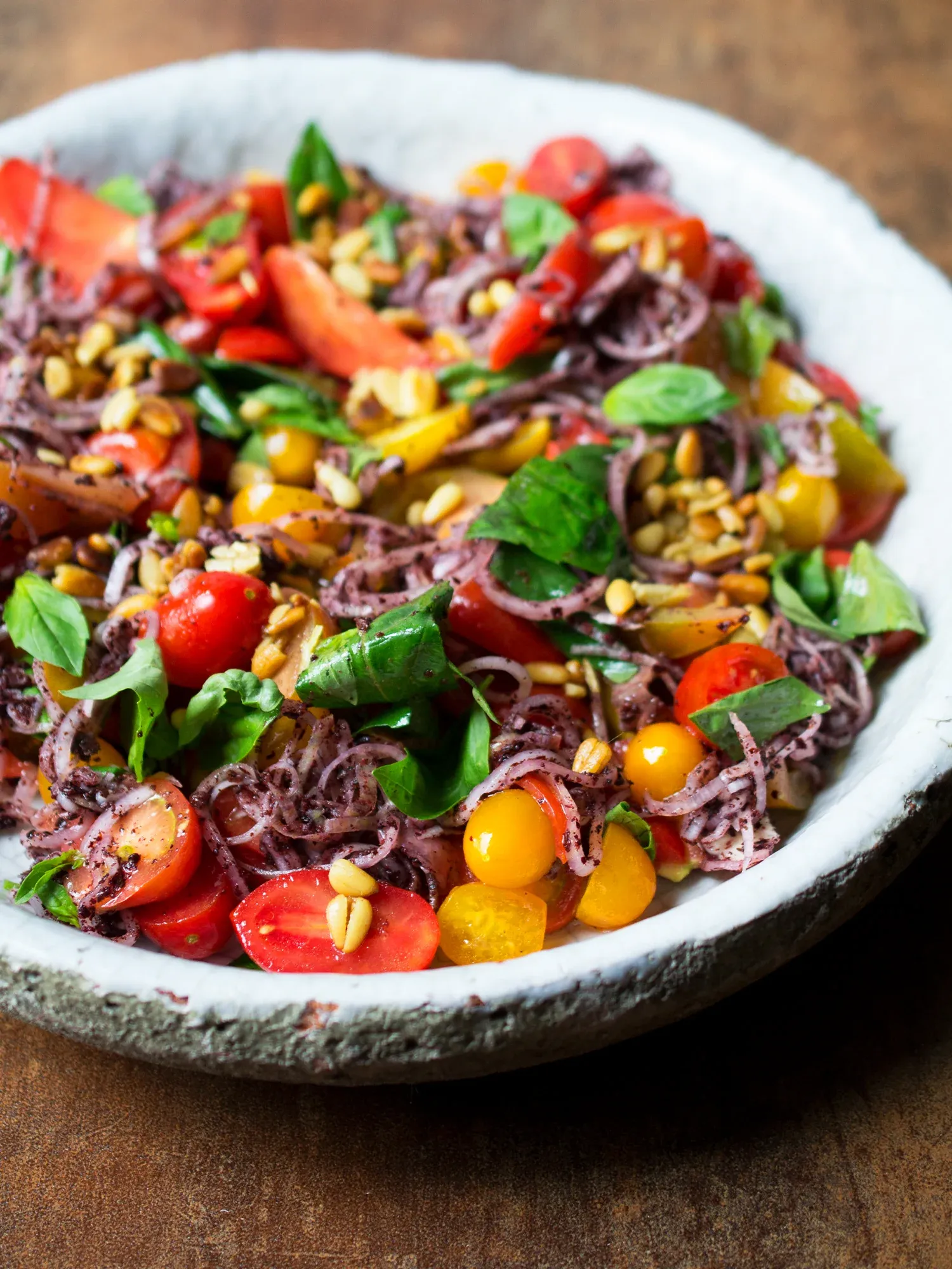 Färgglad sallad med körsbärstomater, rödlök, basilika och rostade pinjenötter i en vit skål