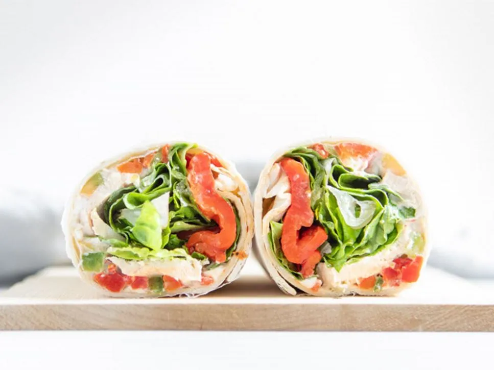 Två halvor av en wrap med sallad, kyckling och röd paprika på en skärbräda